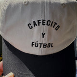 Cap with 'Cafecito y Futbol' text on a blurred background