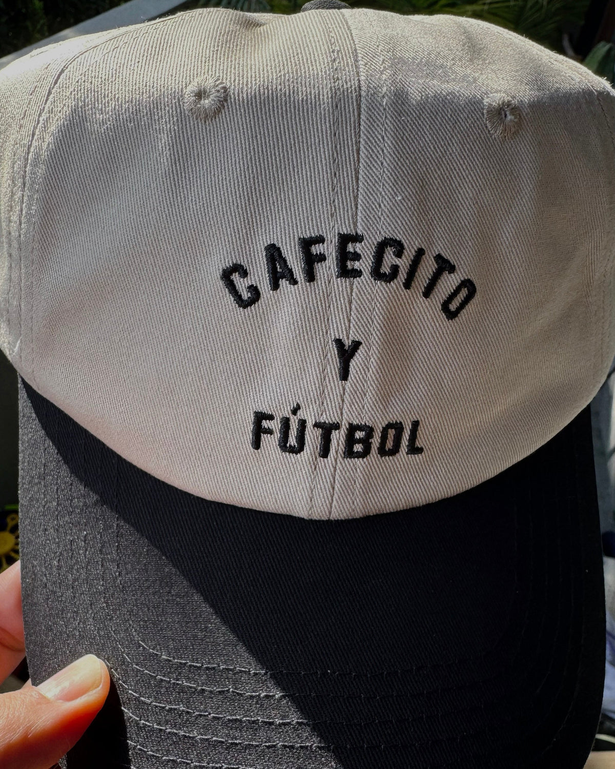 Cap with 'Cafecito y Futbol' text on a blurred background